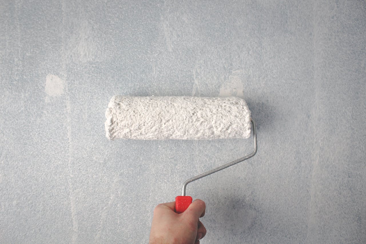 about-02 A person's hand using a paint roller to apply white paint on a wall.