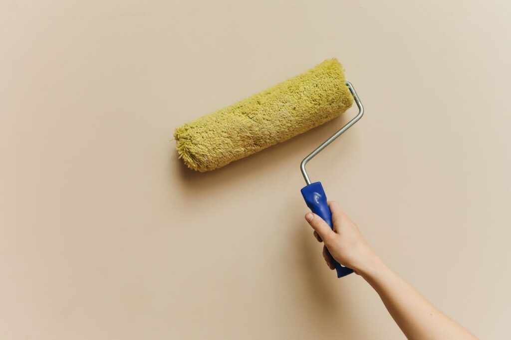 pexels photo 5583126 A hand using a yellow paint roller to paint a beige wall. Perfect for DIY and home improvement themes.
