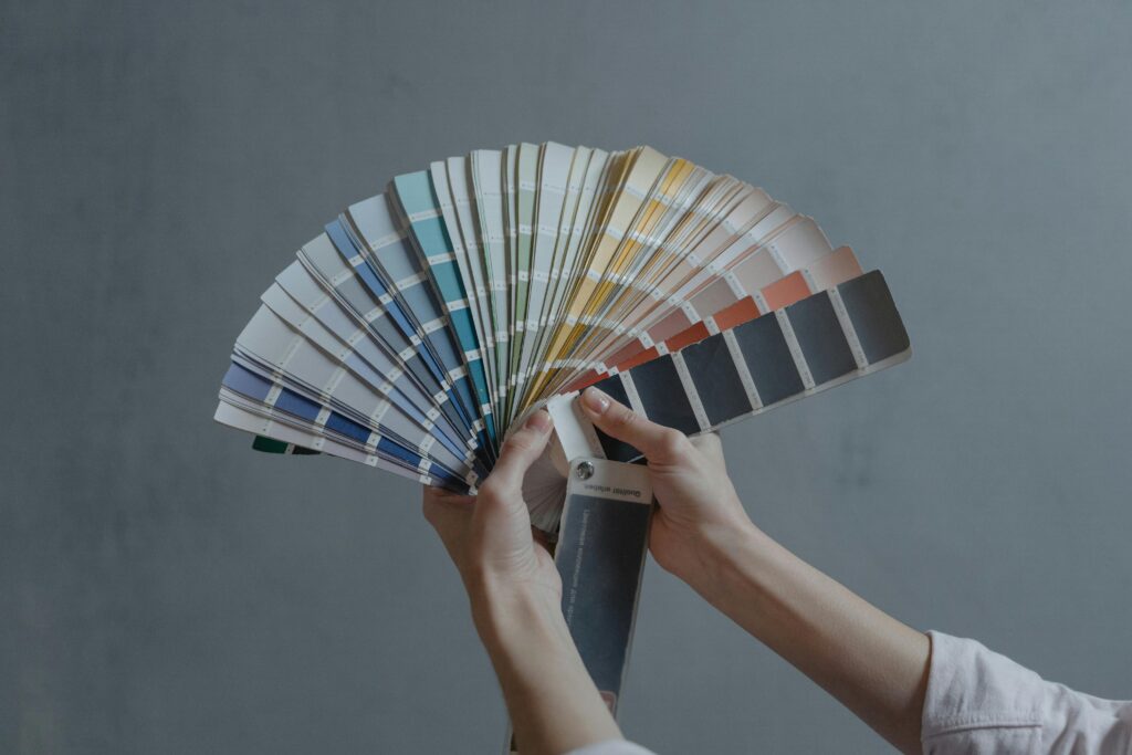 pexels photo 6474450 6474450 Hands holding a colorful fan of swatches on a gray backdrop, ideal for design themes.